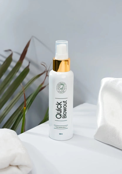 Quick Blowout Heat Defence Spray bottle on a white surface with palm leaves in the background.