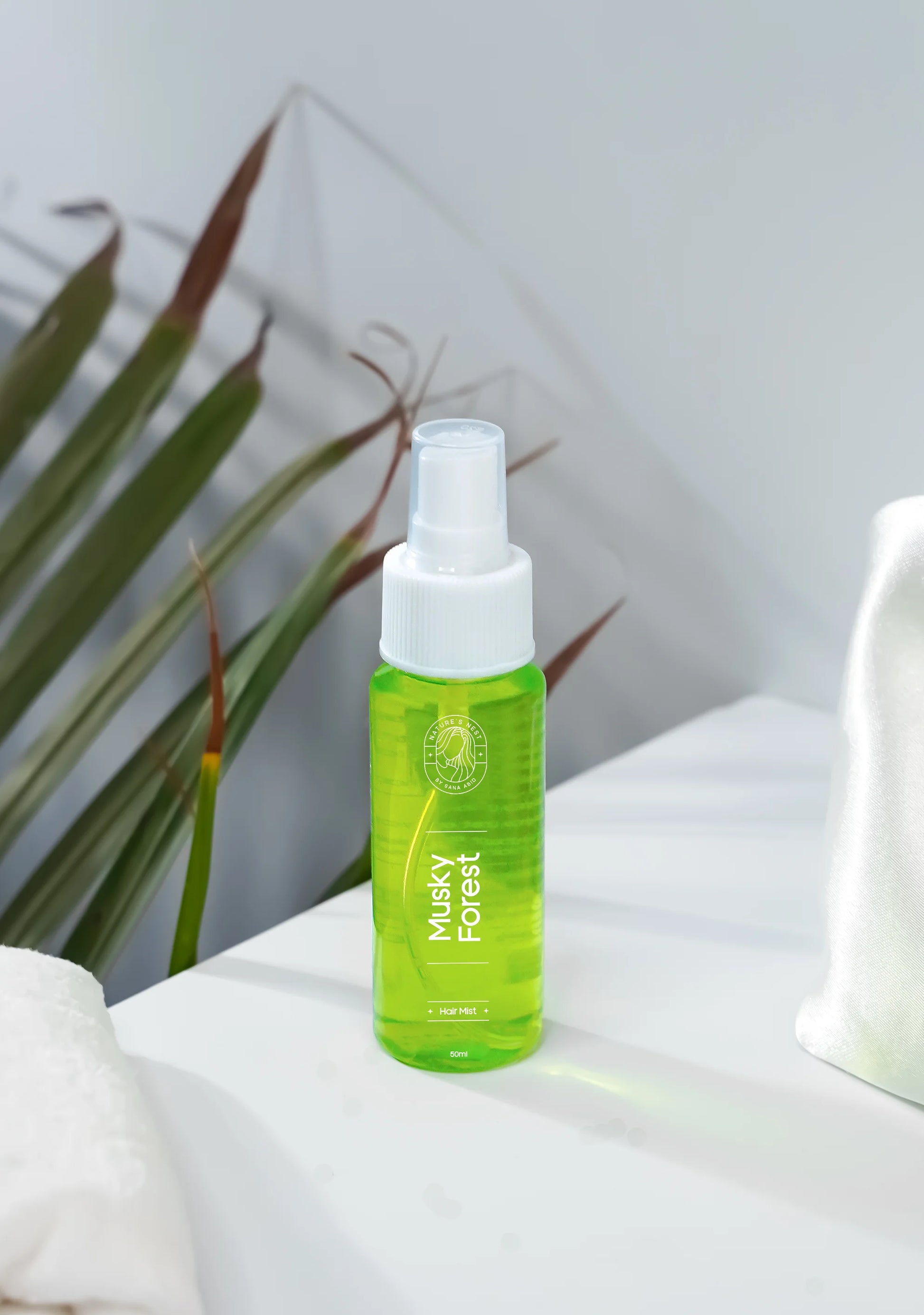 Musky Forest Hair Mist bottle on a white surface with green leaves in the background, promoting luxury hair care.